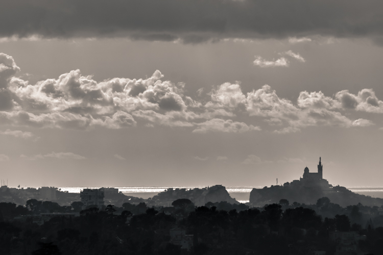 Notre-Dame de la Garde photographiée depuis hauteurs dAllauch sous un ciel nuageux laissant apparaitre par endroit la lumière du soleil.