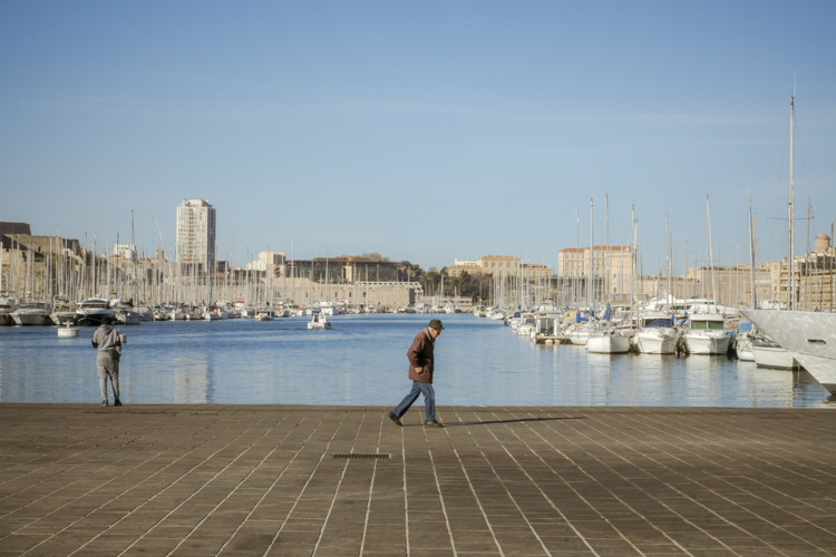 Un vieil homme portant un chapeau, marchant sur le Vieux-Port � Marseille, semble porter toute la mis�re du monde sur les �paules  