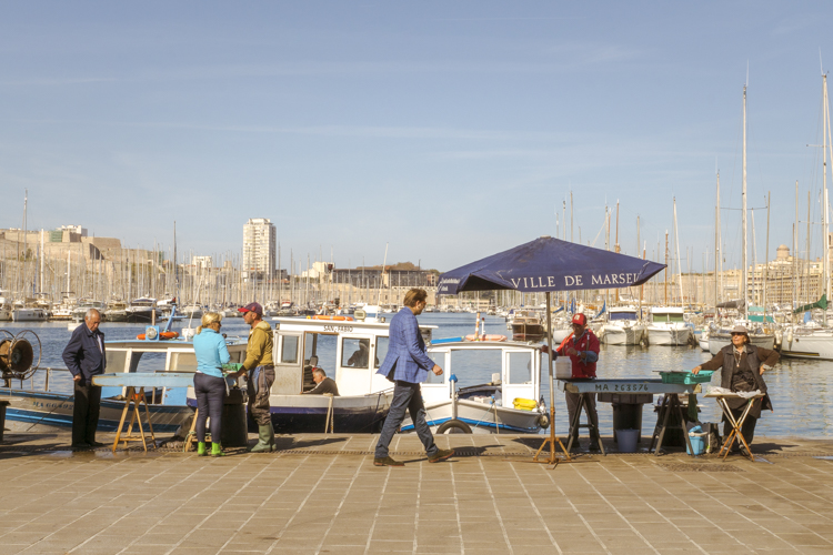 Un homme en costume se dirige vers un étal de poisson sur le Vieux-Port à Marseille.