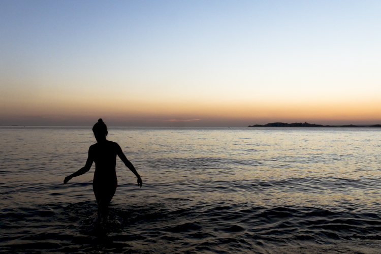 Une jeune fille sort de l'eau au coucher du soleil.