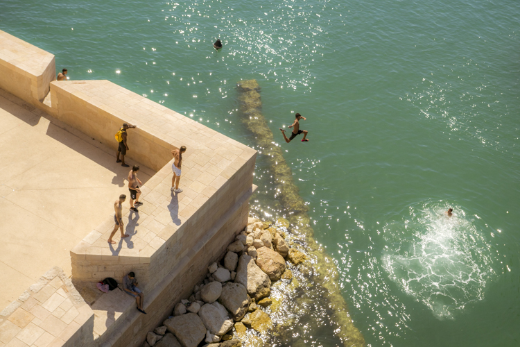 Un jeune garçon saute dans la Méditerranée à partir des remparts en contre-bas du Fort Saint-Jean sous le regard des ses camarades de jeu.