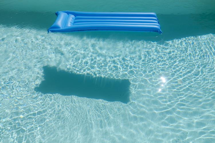 Un matelas pneumatique bleu flotte seul dans une piscine.