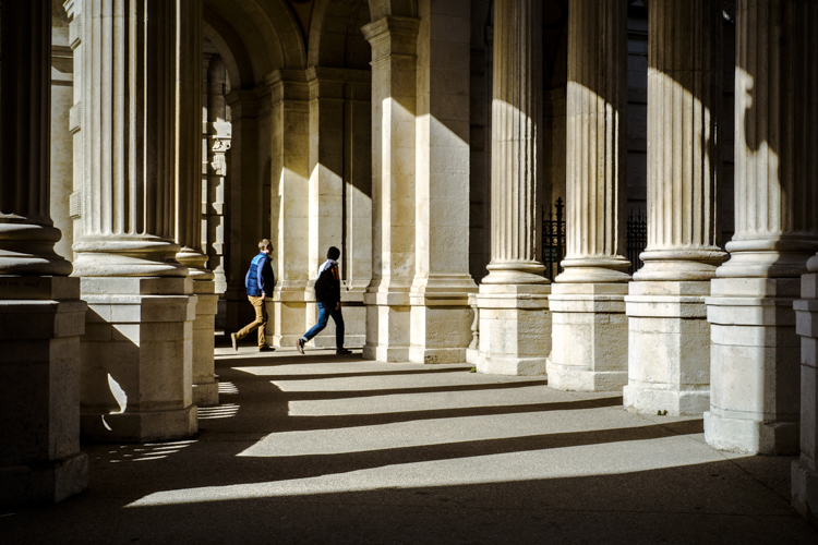 Deux hommes marchent sous les colonnades du Palais Longchamp.