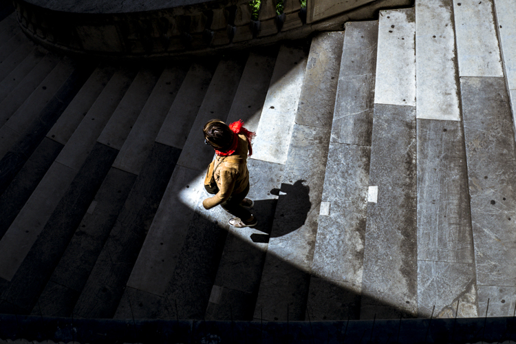 Une dame descendant un escalier entre ombre et lumière au Palais Longchamp à Marseille photographiée de dessus , du haut de cet escalier.