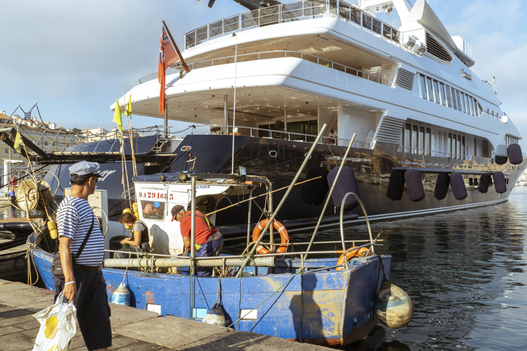 Une petit bateau de pêche décharge sa production du jour amarré au Vieux-Port à Marseille juste à côté d'un yacht luxueux.