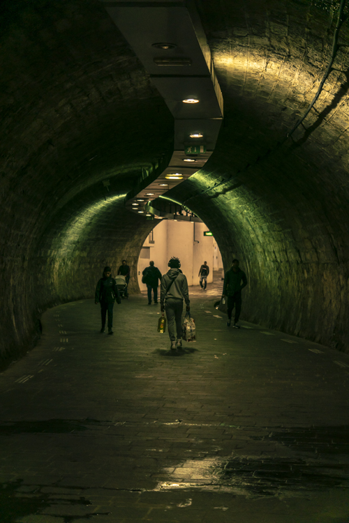 Des passants dans la pénombre du tunnel à la sortie de la station de métro Noailles à Marseille.